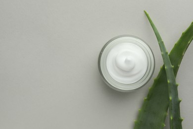 Jar with cream and aloe leaves on light grey background, flat lay. Space for text