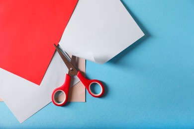 Photo of Red scissors and color sheets of paper on light blue background, flat lay