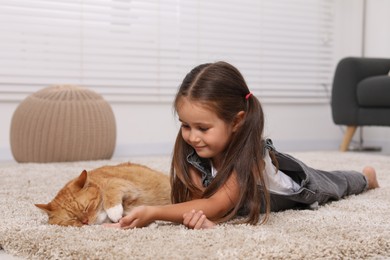 Photo of Smiling little girl and cute ginger cat on carpet at home
