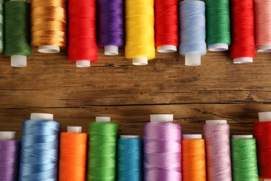 Photo of Different colorful sewing threads on wooden background, flat lay. Space for text