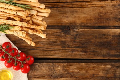 Photo of Delicious grissini sticks, oil, rosemary and tomatoes on wooden table, flat lay. Space for text