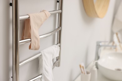 Photo of Heated towel rail with underwear on white wall in bathroom, closeup