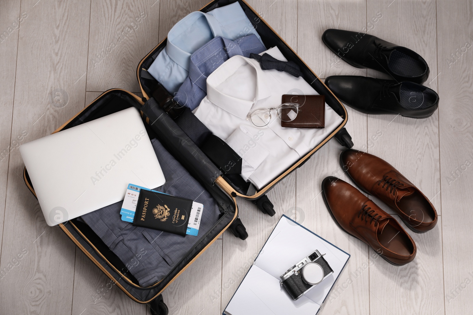 Photo of Open suitcase with men's clothes, accessories and shoes on floor, flat lay