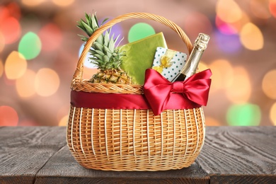 Image of Wicker basket full of gifts on wooden table against blurred festive lights 