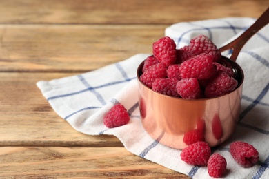Photo of Saucepan with delicious ripe raspberries on wooden table, space for text