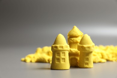 Photo of Castle figures made of yellow kinetic sand on grey background, closeup. Space for text