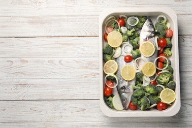 Photo of Raw fish with vegetables and lemon in baking dish on wooden table, top view. Space for text