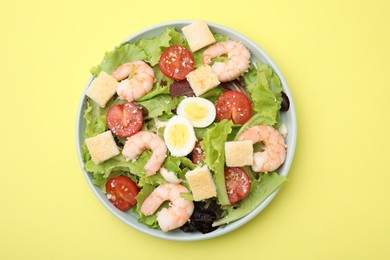 Photo of Delicious Caesar salad with shrimps on yellow background, top view