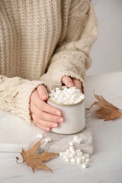 Woman in autumn sweater holding hot cozy drink at table