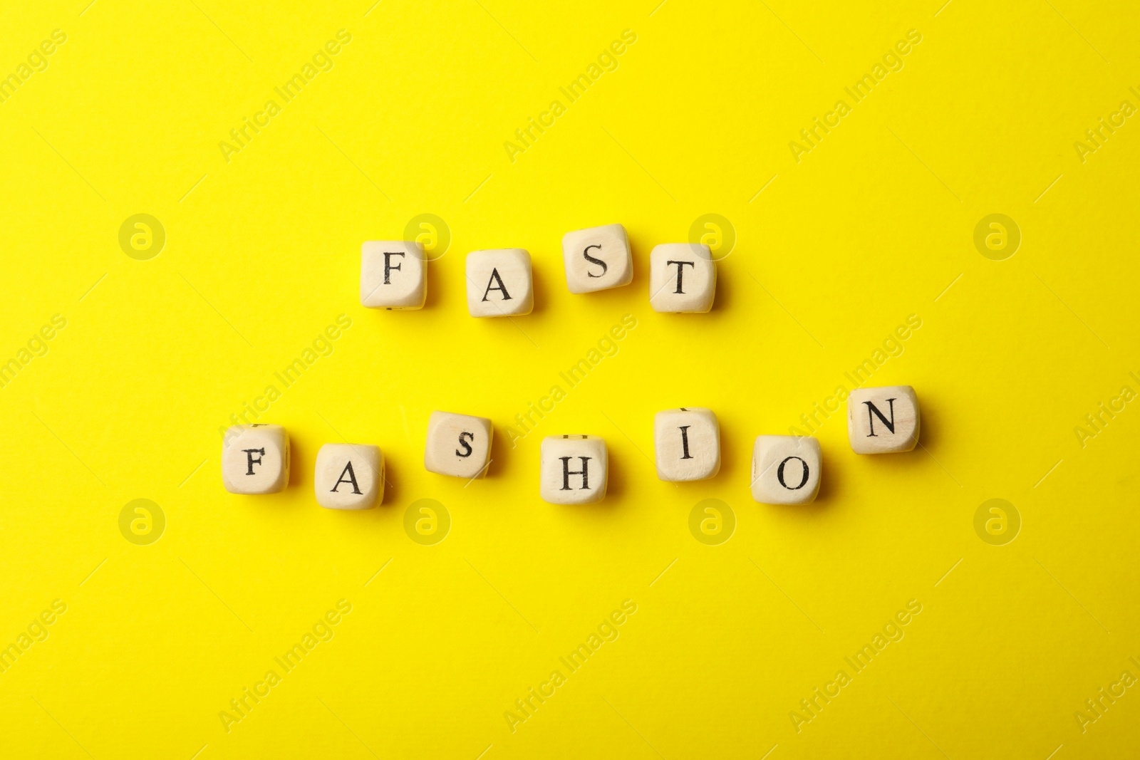 Photo of Wooden cubes with phrase Fast Fashion on yellow background, flat lay