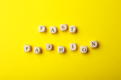 Photo of Wooden cubes with phrase Fast Fashion on yellow background, flat lay