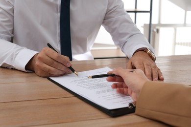 Photo of Businesspeople working with contract at wooden table indoors, closeup