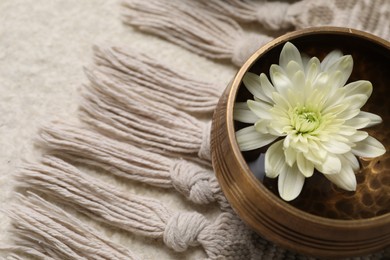 Photo of Tibetan singing bowl with water and beautiful chrysanthemum flower on table, above view. Space for text