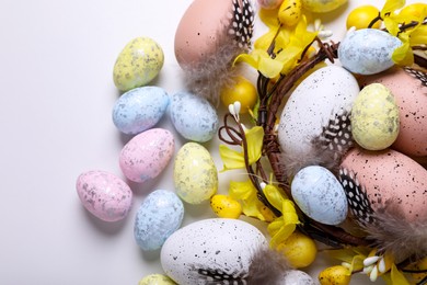 Photo of Decorative nest with many painted Easter eggs on white background, flat lay