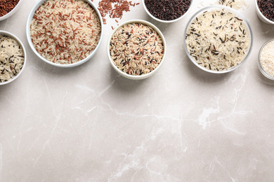 Photo of Different sorts of rice on light grey marble table, flat lay. Space for text