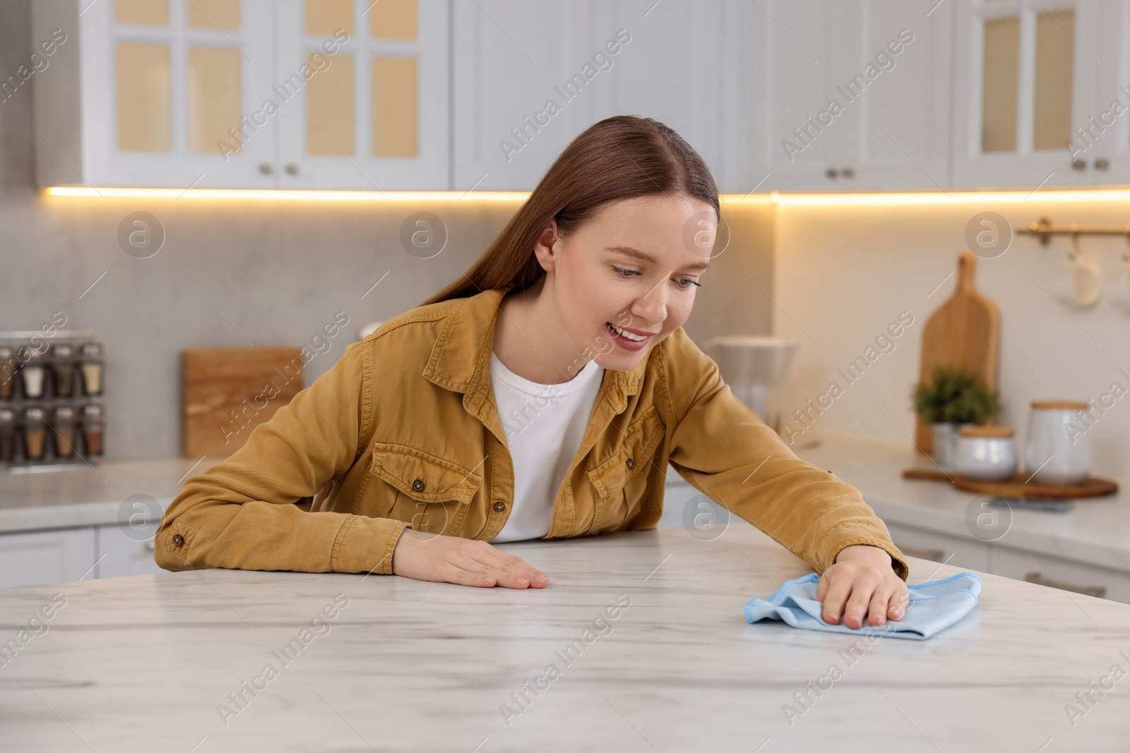 Photo of Woman with microfiber cloth cleaning white marble table in kitchen