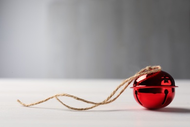 Red sleigh bell with rope on white table. Space for text