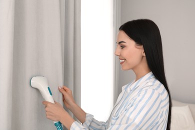 Photo of Woman steaming curtain near window at home