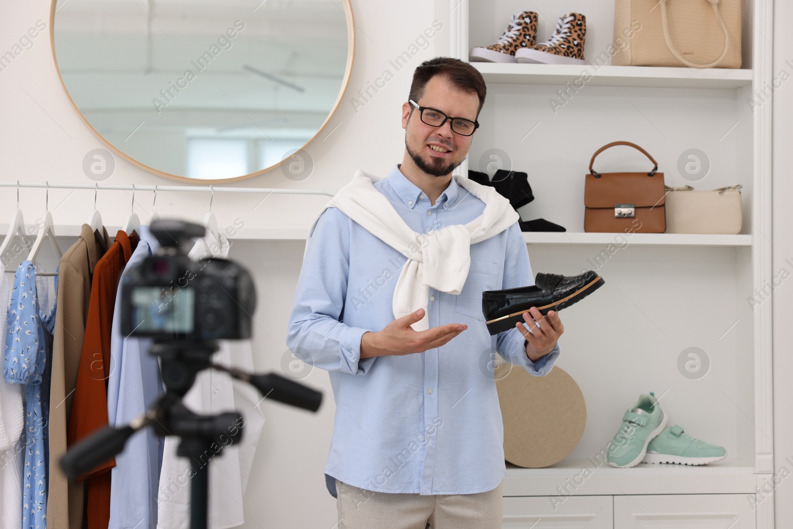 Photo of Smiling fashion blogger showing shoe while recording video at home