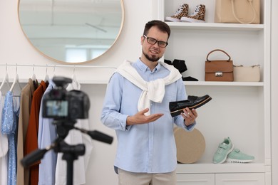 Photo of Smiling fashion blogger showing shoe while recording video at home