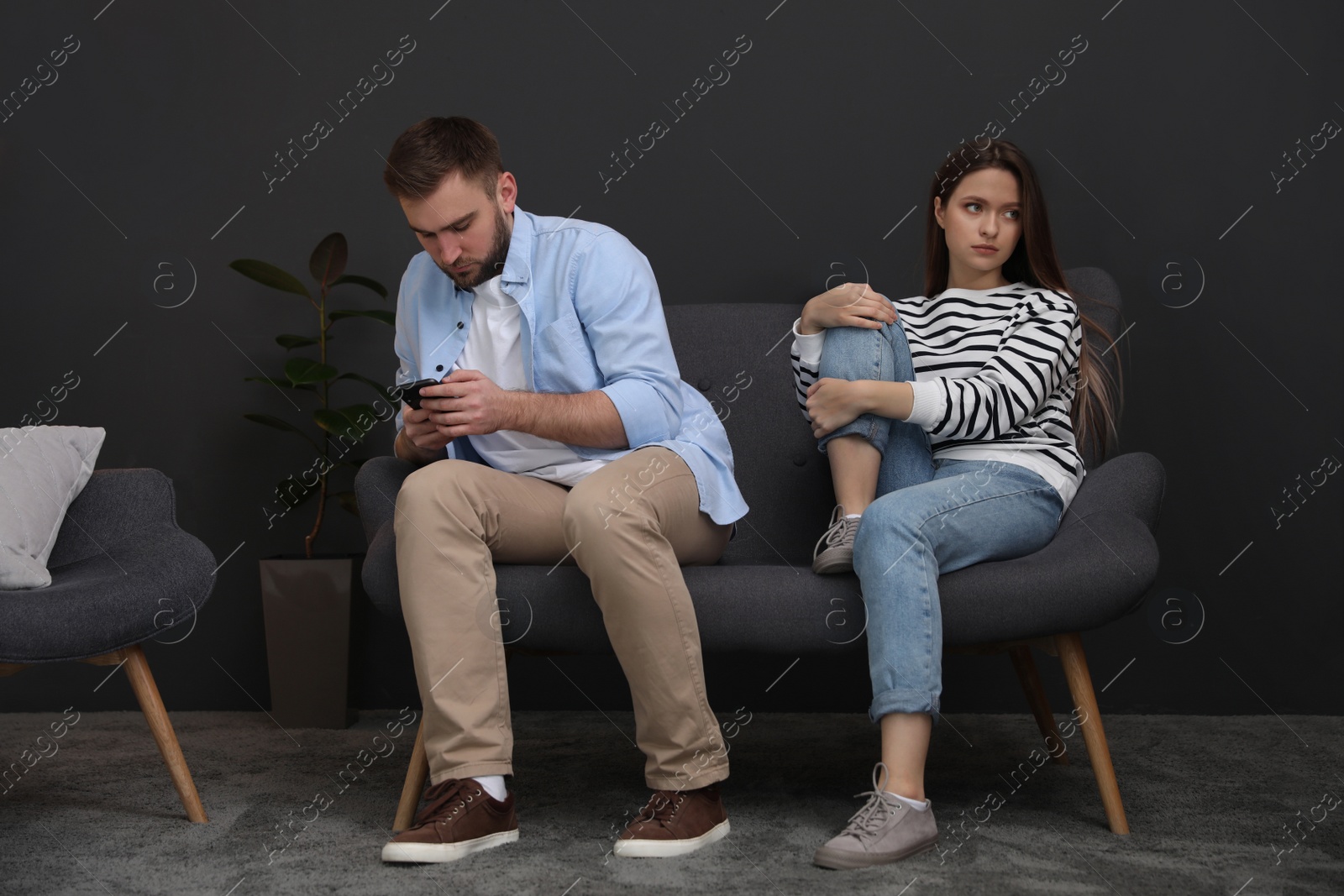 Photo of Young man preferring smartphone over his girlfriend at home. Relationship problems