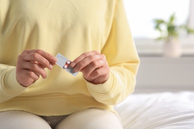 Photo of Woman holding blister of emergency contraception pills in bedroom, closeup
