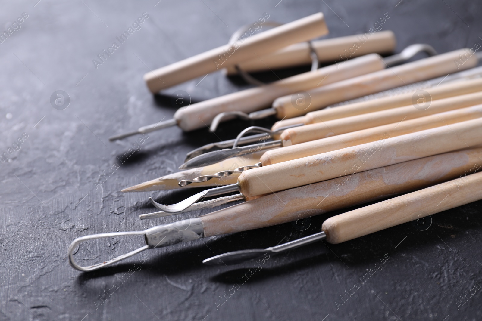 Photo of Set of different clay crafting tools on black table, closeup