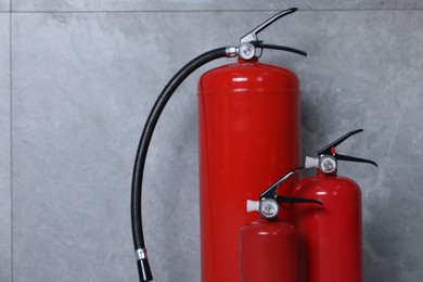 Fire extinguishers near grey wall, space for text