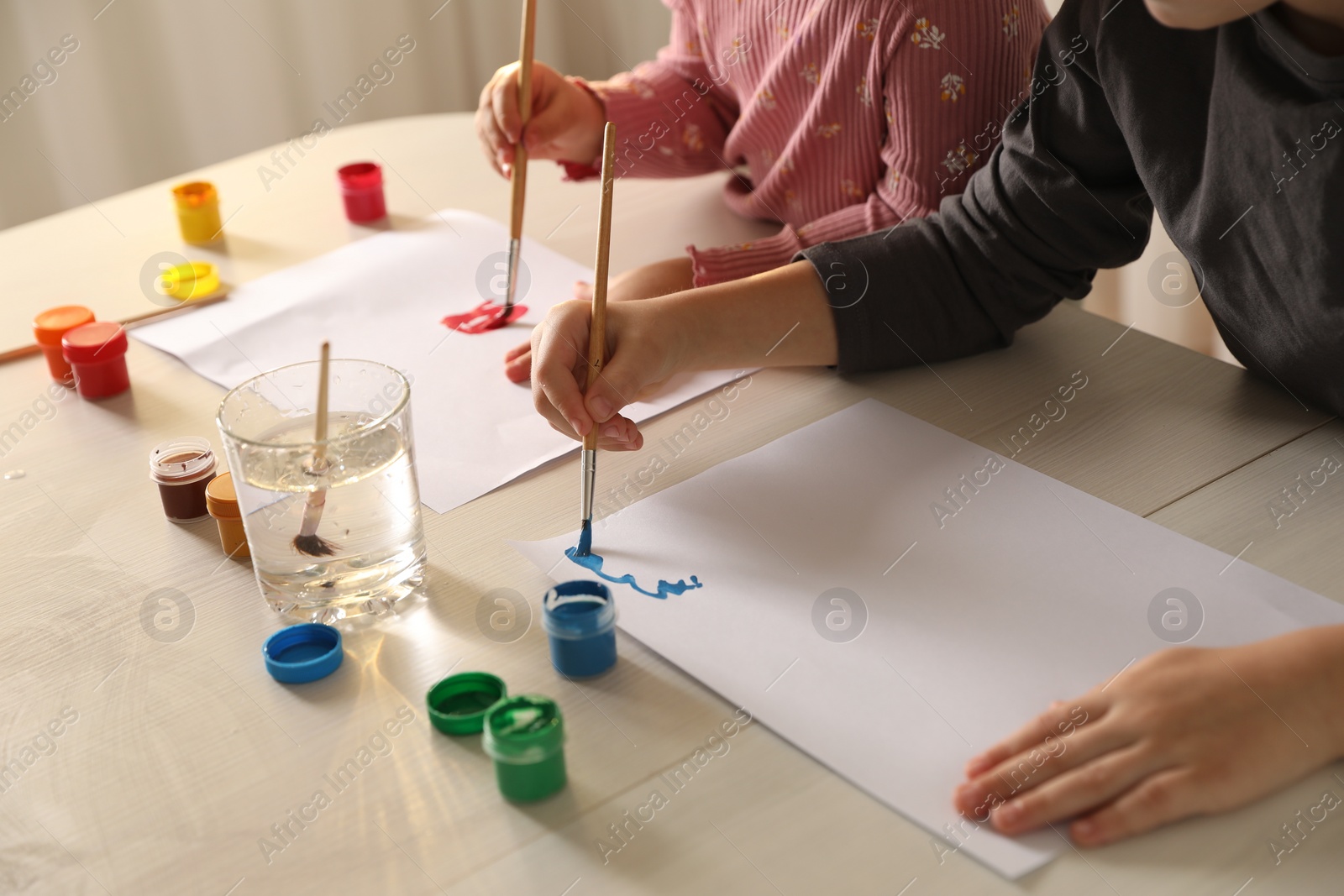 Photo of Little children drawing with brushes at wooden table indoors, closeup