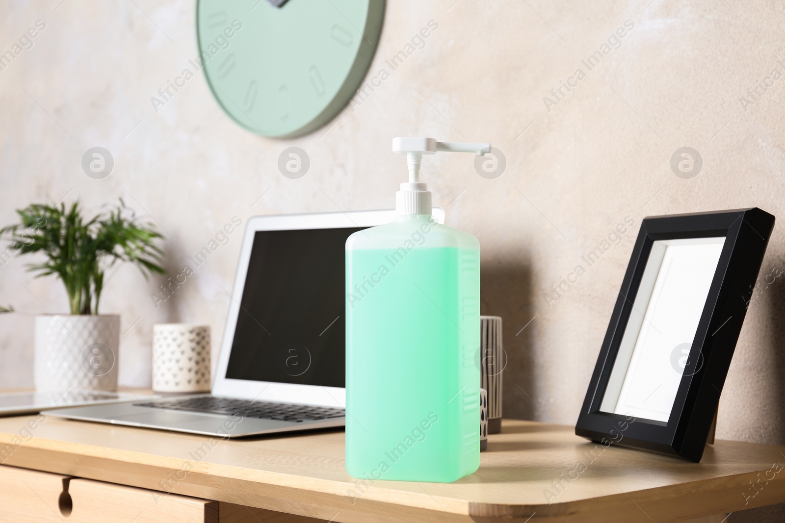 Photo of Dispenser bottle with green antiseptic gel on table in office