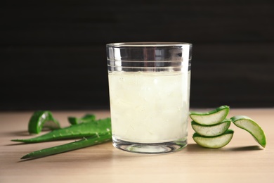 Photo of Glass with aloe vera juice and green leaves on wooden table against dark background