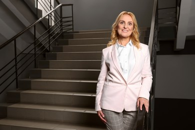 Photo of Happy lady boss near staircase indoors, space for text. Successful businesswoman