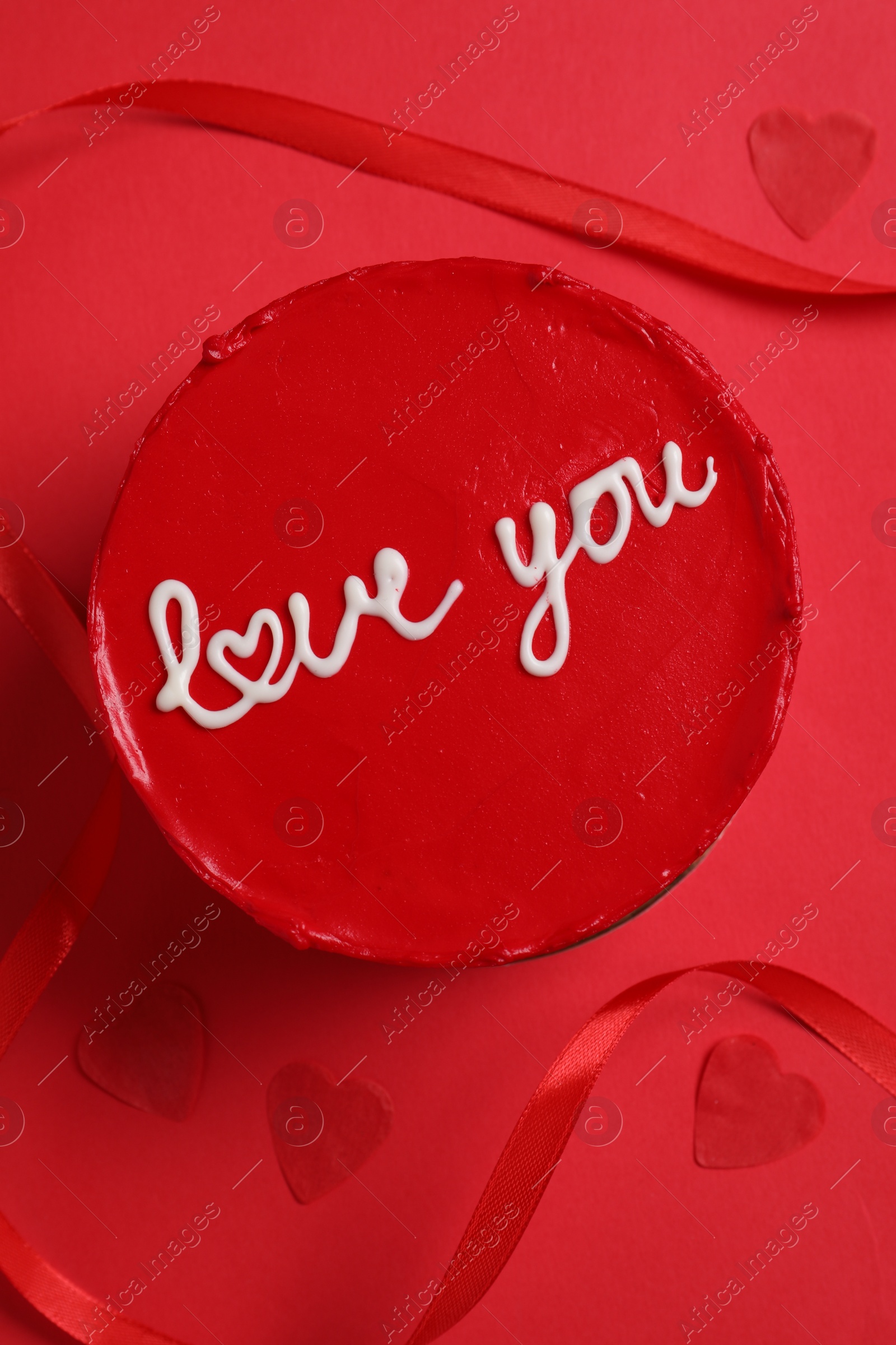 Photo of Bento cake with text Love You, ribbon and paper hearts on red table, flat lay. St. Valentine's day surprise