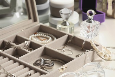 Photo of Jewelry box with many different accessories, perfumes and jars of cosmetic products on white table, closeup
