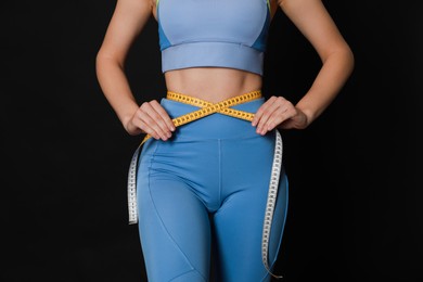 Photo of Woman in sportswear measuring waist with tape on black background, closeup