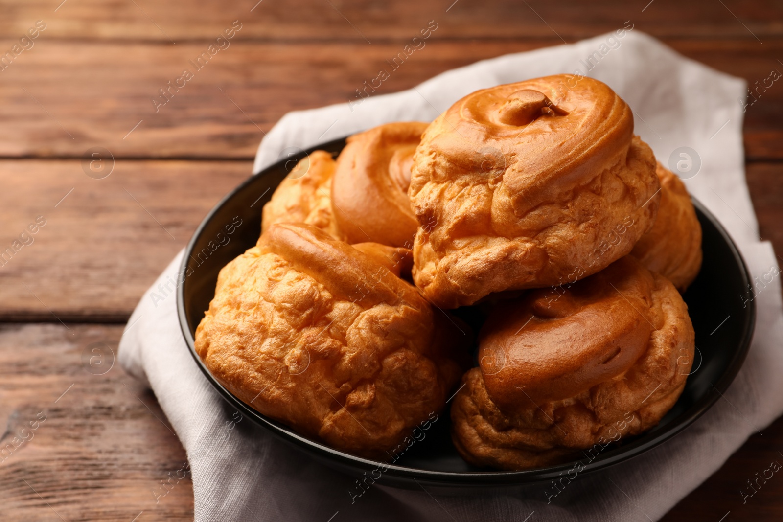 Photo of Plate with delicious profiteroles on wooden table