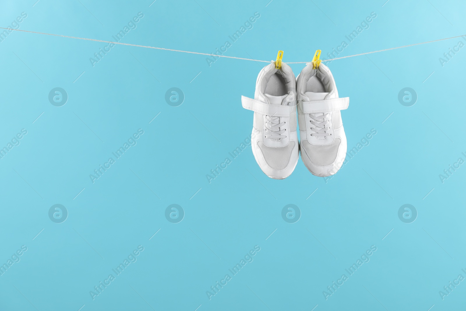 Photo of Stylish sneakers drying on washing line against light blue background, space for text