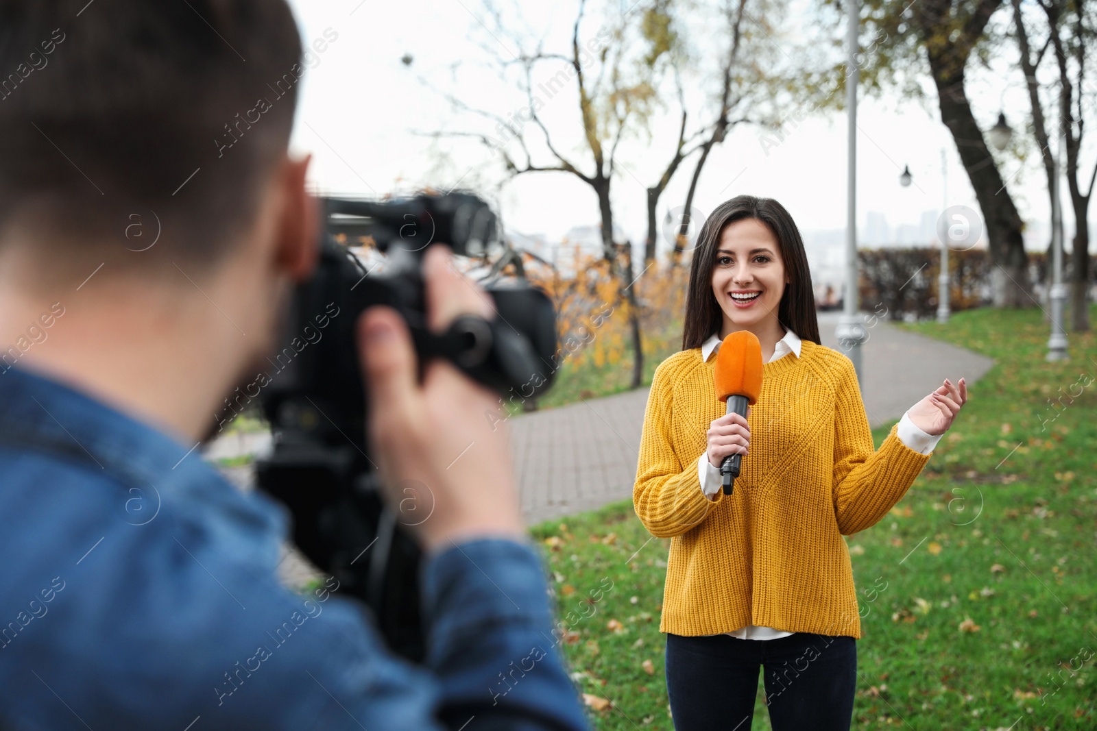 Photo of Young journalist and video operator working in park