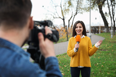 Photo of Young journalist and video operator working in park