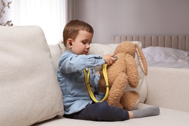 Photo of Cute little boy playing with stethoscope and toy bunny at home. Future pediatrician