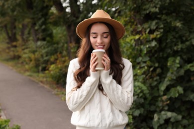 Photo of Beautiful young woman in stylish warm sweater holding paper cup of coffee outdoors