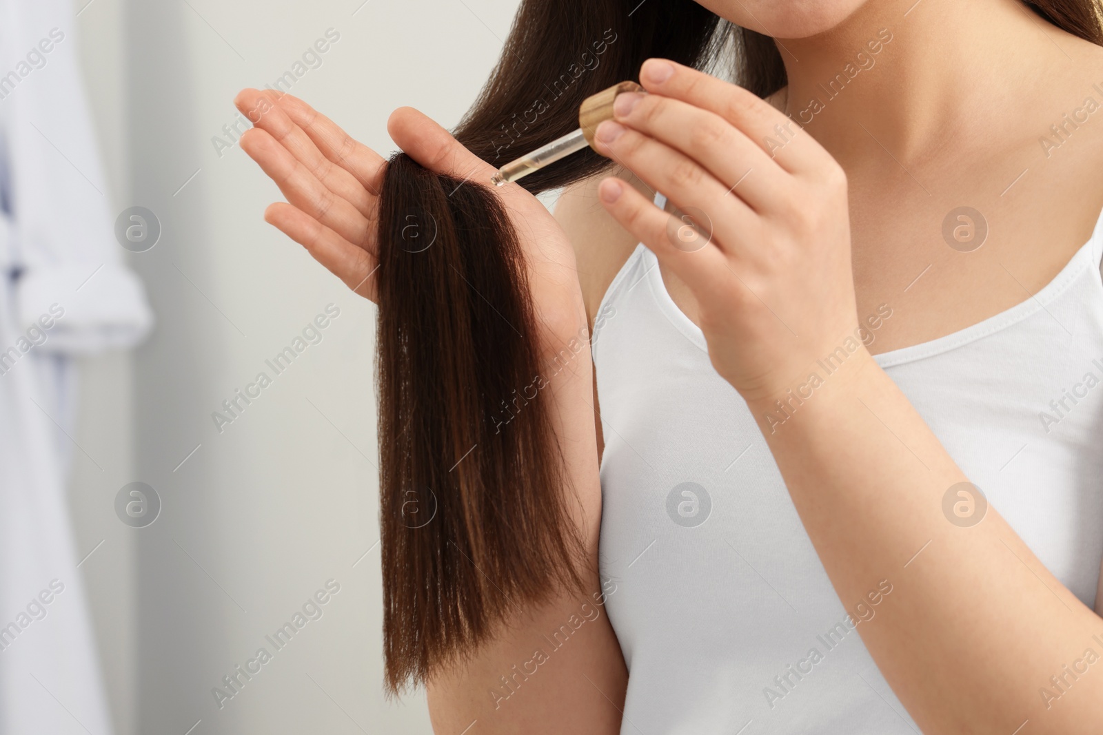 Photo of Woman applying essential oil onto hair on blurred background, closeup