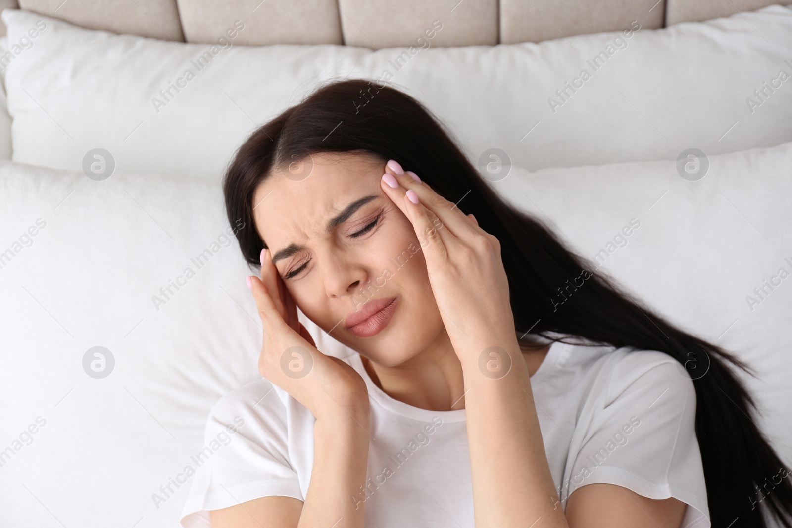 Photo of Young woman suffering from migraine in bed, above view