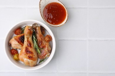 Photo of Marinade, roasted chicken drumsticks, rosemary and tomatoes on white tiled table, flat lay. Space for text