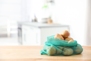 Photo of Net bag with potatoes on wooden table in kitchen, space for text