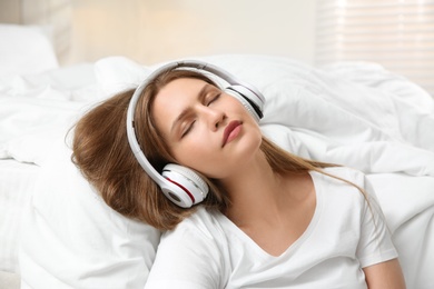 Lazy young woman with headphones sleeping in bedroom