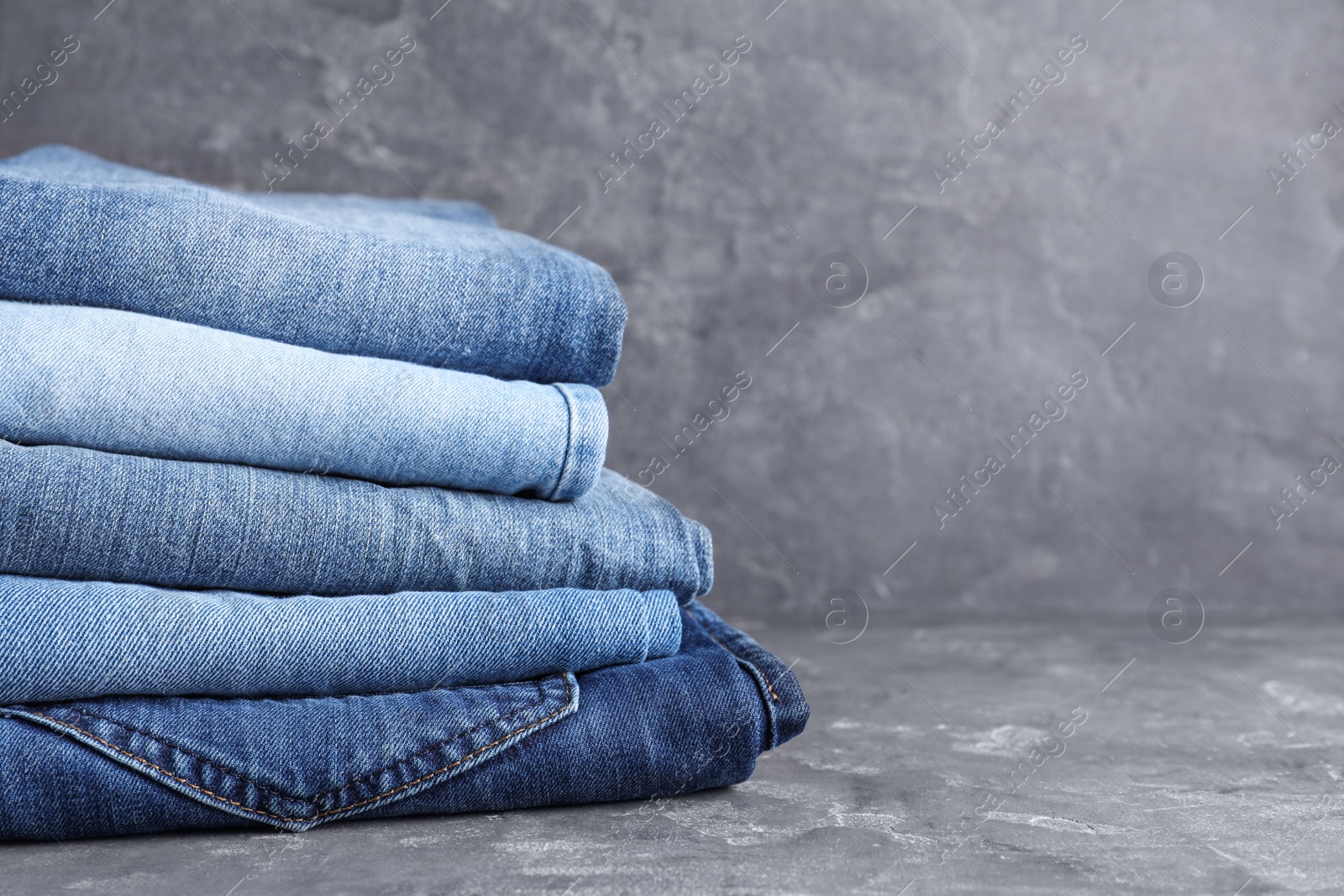 Photo of Stack of different jeans on grey table, space for text