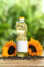 Sunflower cooking oil, seeds and yellow flowers on wooden table outdoors