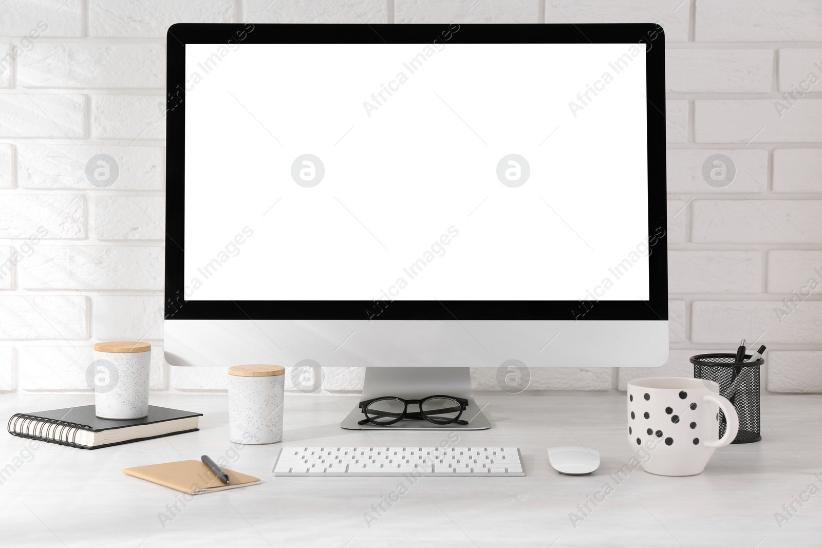 Photo of Office workplace with computer, cup and stationery on light table near white brick wall