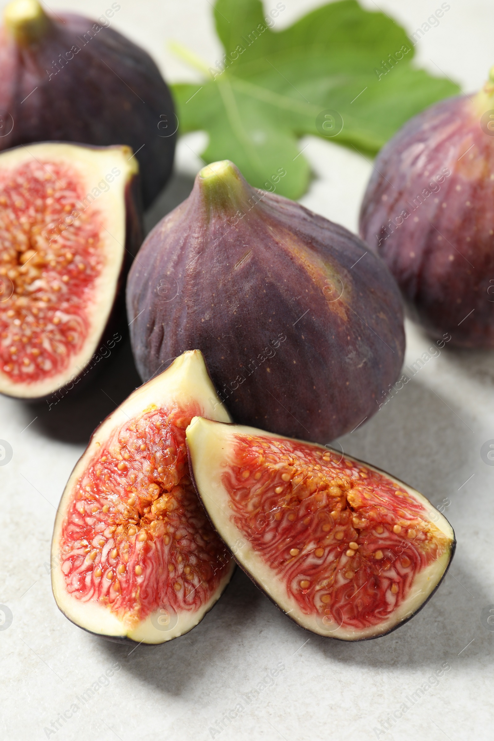 Photo of Fresh ripe figs and green leaf on light table, closeup